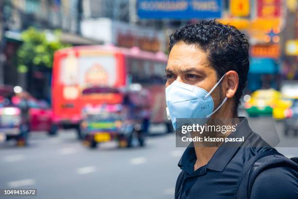 portrait of a man using pm 2.5 pollution mask in the street of a big city . - particule stock-fotos und bilder