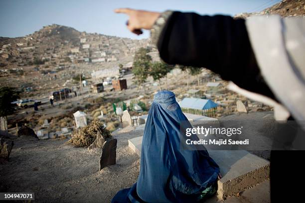 Burqa-covered woman reads the Sura Al-Fatiha verse of the Koran over the grave of a relative in the graveyard October 7, 2010 of Kabul's Saghi...