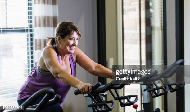 senior woman exercising in a gym - spinning bikes stock pictures, royalty-free photos & images