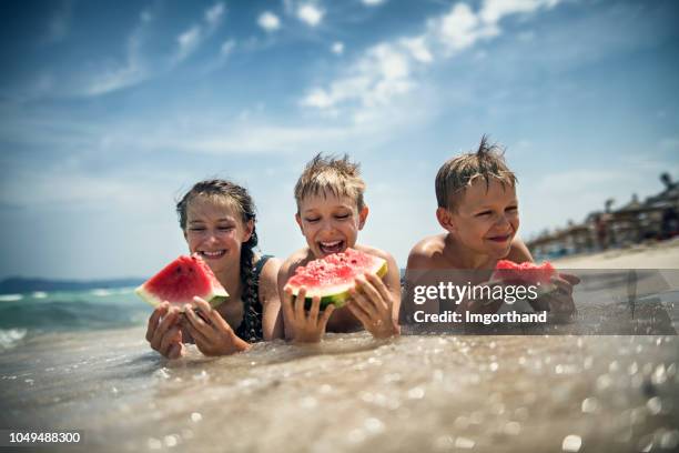 glückliche kinder essen wassermelone am strand - wassermelone stock-fotos und bilder