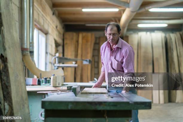 der senior 60 jahre alten mann, der tischler, arbeiten mit der kommerziellen kreissäge-maschine bei der kleinen möbelfabrik - 55 years old stock-fotos und bilder