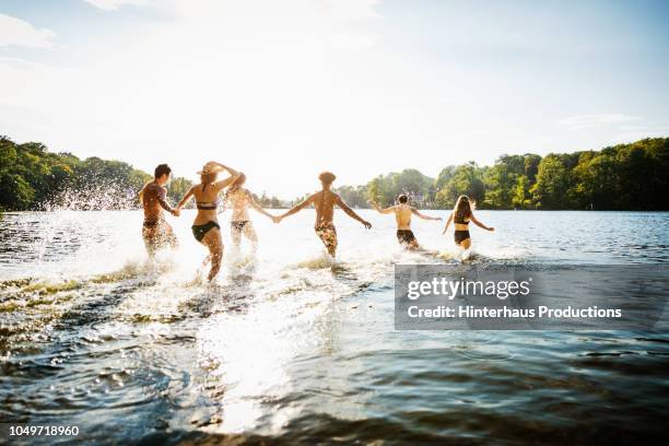 friends wading into lake in summer sun - asian water splash stock-fotos und bilder
