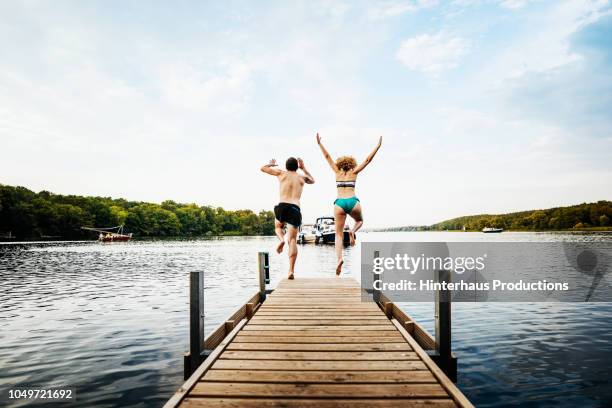 two friends jumping off pier together - ponton photos et images de collection