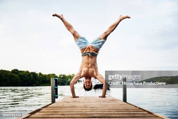 man smiling while doing handstand on lake pier - bootssteg stock-fotos und bilder