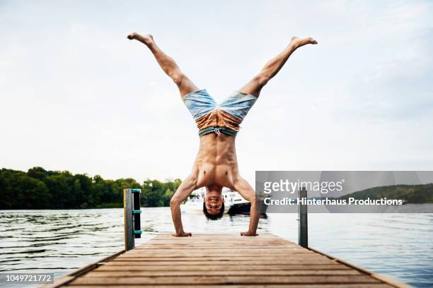 man smiling while doing handstand on lake pier - swimwear stockfoto's en -beelden