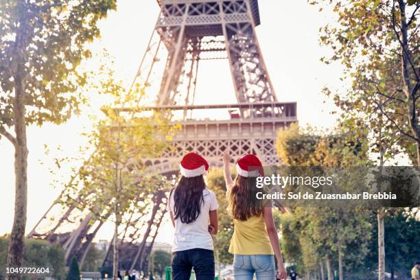 teenager sisters traveling together with christmas hats. the younger one is excited to see the eiffel tower. - eiffel tower christmas stock pictures, royalty-free photos & images