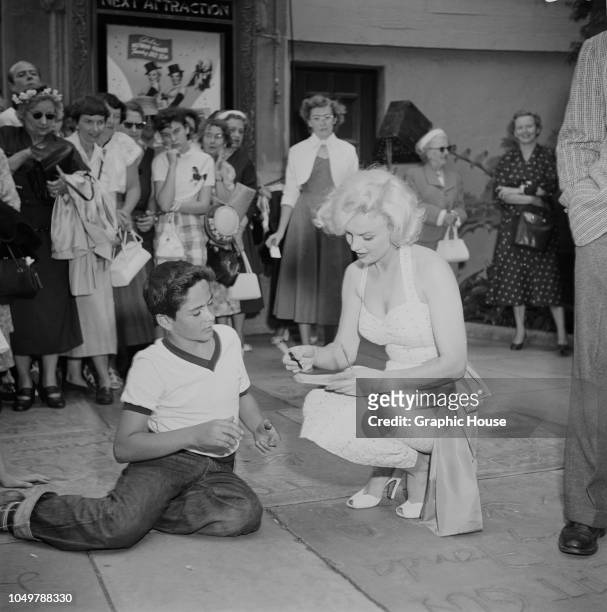 American actress Marilyn Monroe signs an autograph for a fan outside Grauman's Chinese Theatre in Hollywood, California, 26th June 1953. Monroe is at...