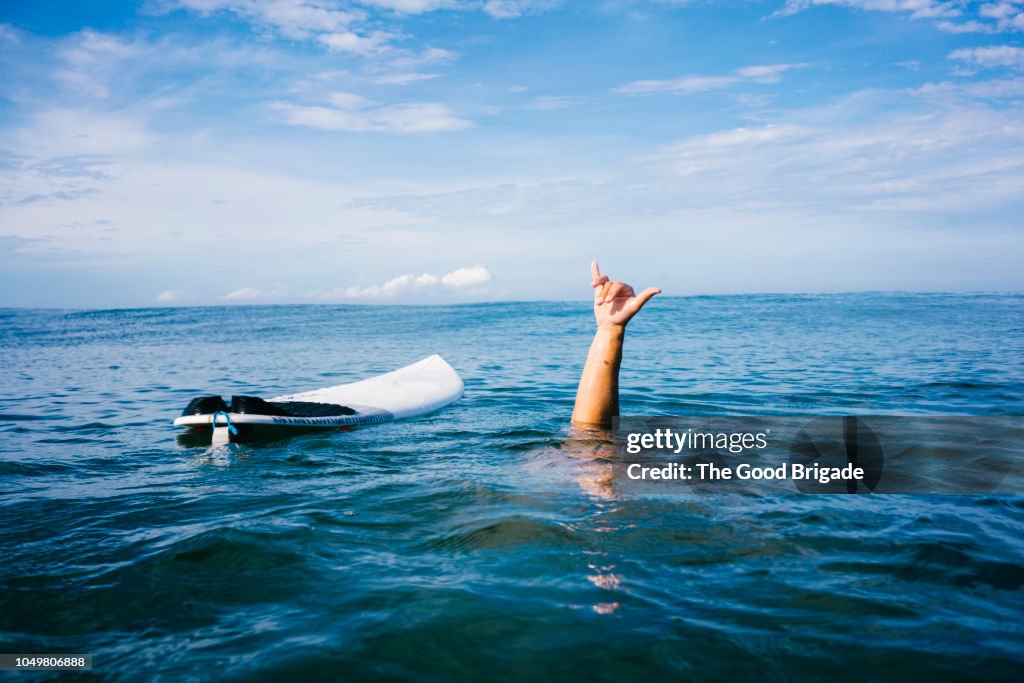Man underwater giving shaka sign near surfboard