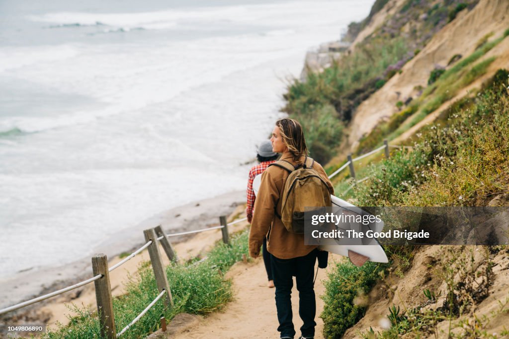 Man carrying a surfboard on path near ocean