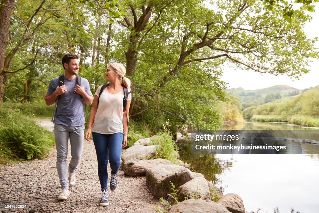 Couple Hiking Along Path By River In UK Lake District