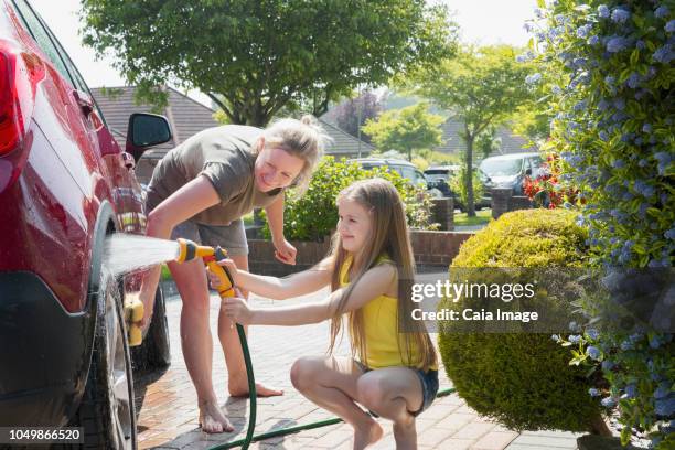 mother and daughter washing car in sunny driveway - girls taking a showering stockfoto's en -beelden