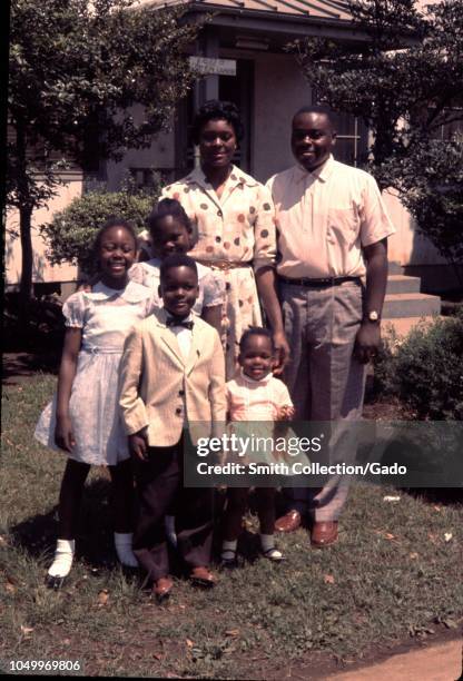 Portrait of African-American family standing in front of their home wearing church clothing, man in formal shirt and pants, woman wearing dotted...