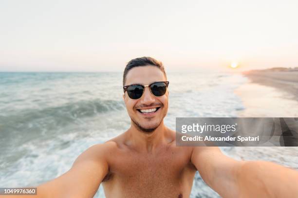 young happy smiling man in sunglasses taking selfie at the beach during sunset - selfie male stock pictures, royalty-free photos & images