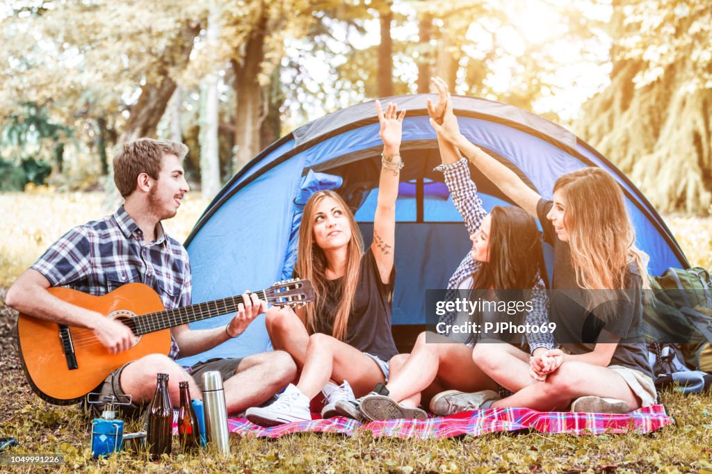 Group of young friends playing guitar and singing at camping