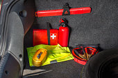 Interior of the trunk of the car in which there is a first aid kit, fire extinguisher, warning triangle, reflective vest, starter cables and tow rope