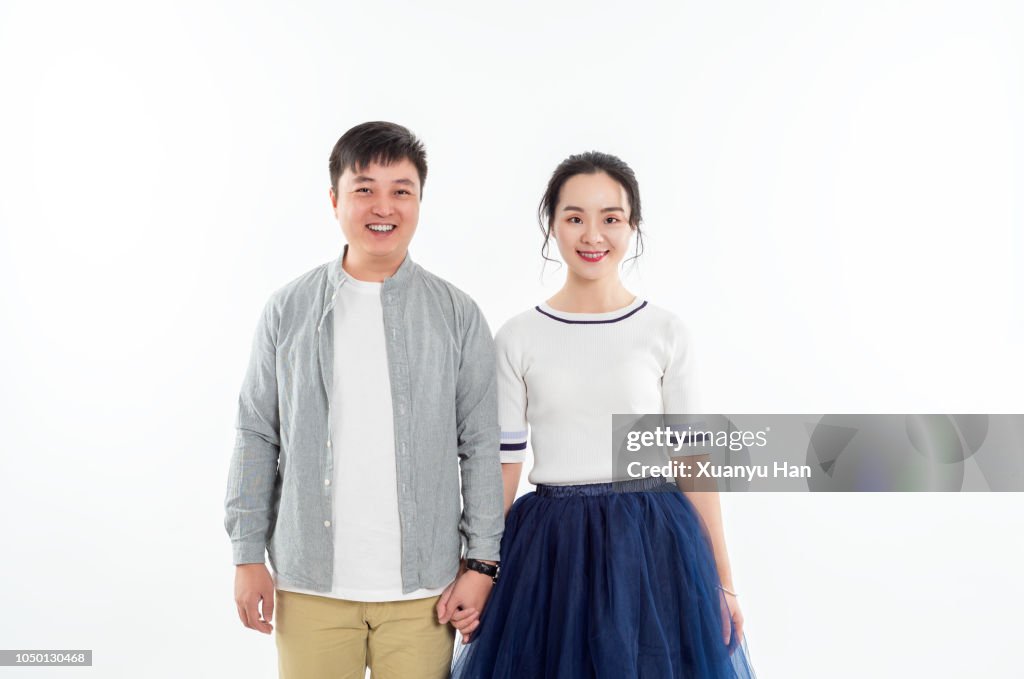 Portrait of couple holding hands while standing against white background