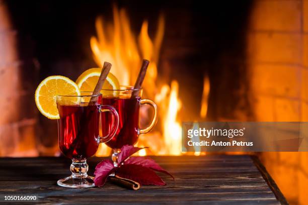 two glasses of hot mulled wine with spices on wooden table against fireplace - ホットワイン ストックフォトと画像
