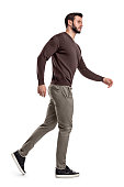 A bearded man in casual garb walks in a side view and looks suspiciously sideways.