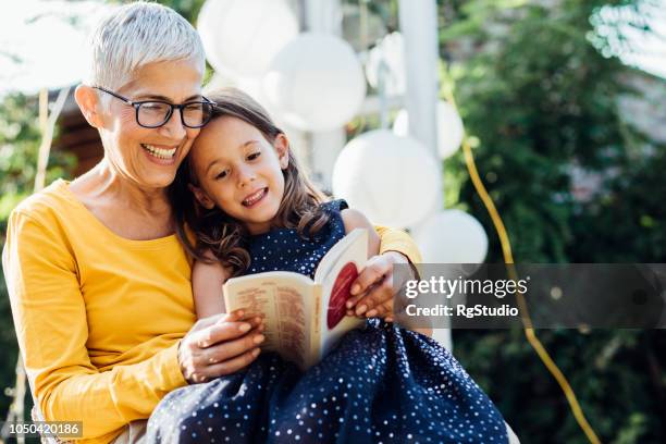 smiling woman reading to granddaughter - grandmother imagens e fotografias de stock