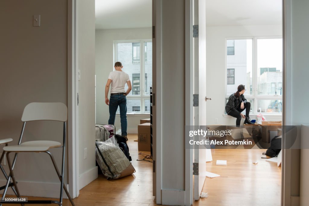 Moving into the new house. Teenage girl sitting in her future room between boxes with her stuff, and the young 28-years-old man looking around the apartment