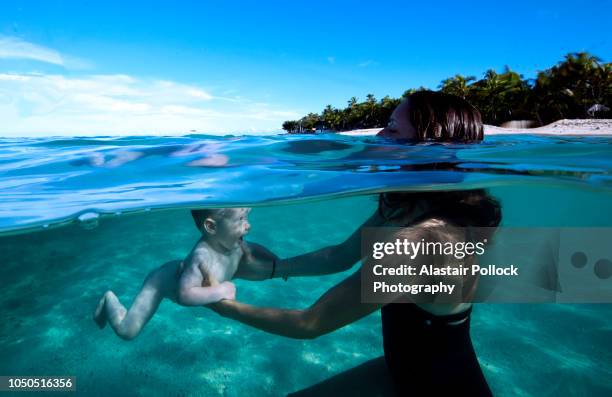 mother swimming with baby at tropical beach - fiji family stock-fotos und bilder