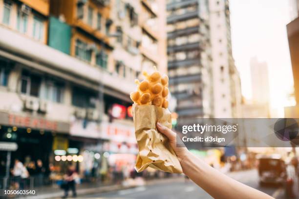 human hand holding freshly made traditional street snack egg waffle against city street in hong kong - cakestand stock-fotos und bilder