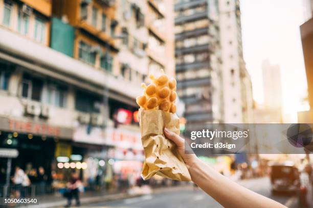 human hand holding freshly made traditional street snack egg waffle against city street in hong kong - cuisine de rue photos et images de collection