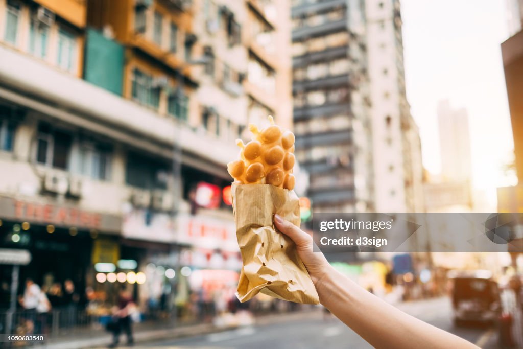 Human hand holding freshly made traditional street snack egg waffle against city street in Hong Kong