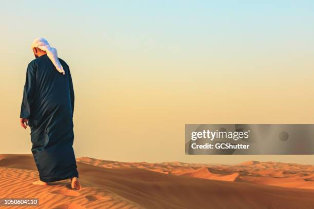 arab man walking barefeet on the sand dunes - dubai desert stock pictures, royalty-free photos & images