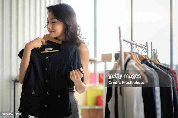 happy asian woman trying coat on in mall or clothing store. - kledingstuk stockfoto's en -beelden