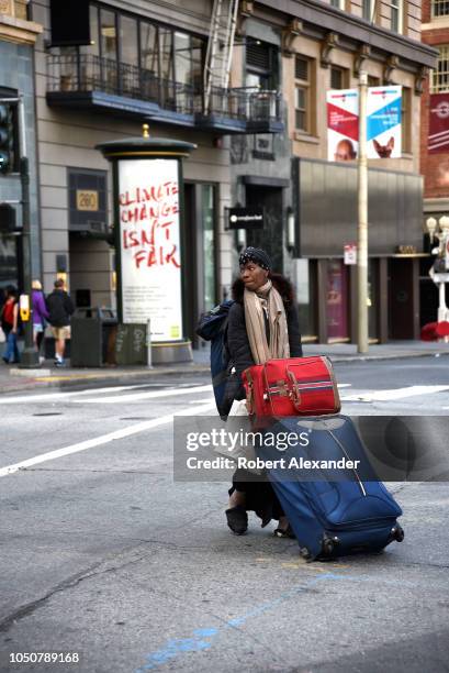 Woman drags her possessions packed into suitcases and a backpack across a busy intersection in San Francisco, California.