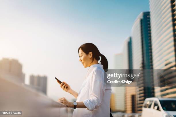 beautiful young asian woman texting on smartphone at outdoor parking lot in downtown city - go red for women fotografías e imágenes de stock