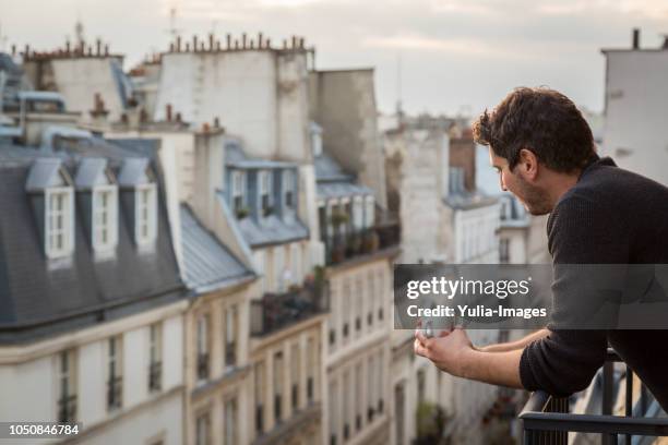 mid adult man holding coffee cup while leaning on balcony railing  paris  france - balcony fotografías e imágenes de stock