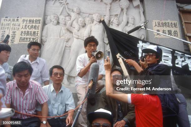 View of demonstrators gathered in Tiananmen Square where singer-composer Hou Dejian speaks through a megaphone; also seen are literary critic Liu...