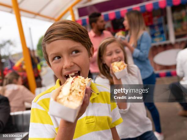 happy kids essen junk-food in einem vergnügungspark - festival food stock-fotos und bilder