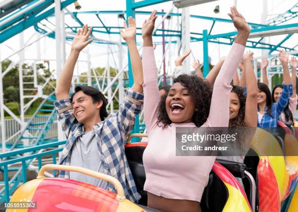 glücklich gruppe von menschen, die spaß in einer achterbahn in einem vergnügungspark - young woman screaming on a rollercoaster stock-fotos und bilder