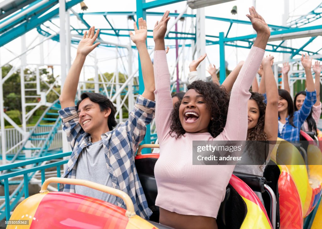 Happy group of people having fun in a rollercoaster at an amusement park