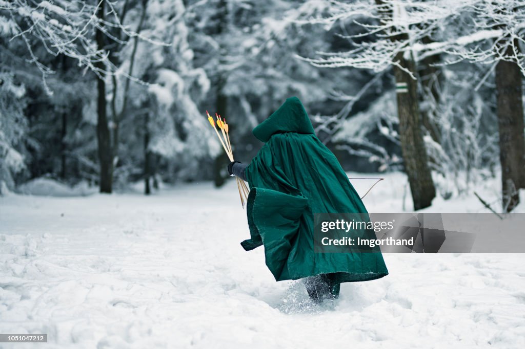 Pequeno arqueiro correndo na floresta de inverno