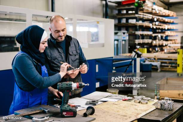 lagarbete: tekniker förklarar ett arbetsredskap till en ung kvinna i en workshop - migration bildbanksfoton och bilder