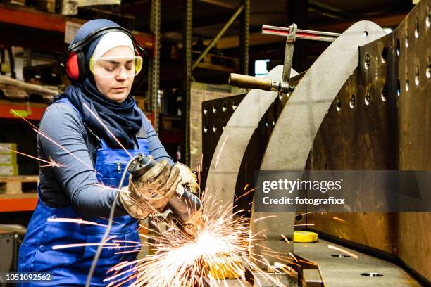 young female trainee works with a grinder in a workshop, flying sparks - factory engineer woman stock pictures, royalty-free photos & images