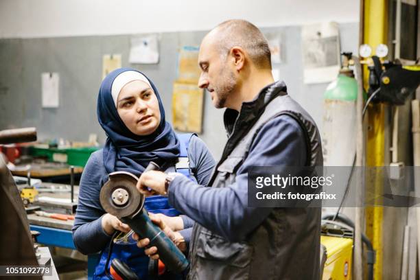 teamwork: technician explains a grinder to a female trainee in a workshop - islamic school stock pictures, royalty-free photos & images