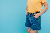 cropped image of girl standing with hands in pockets isolated on blue