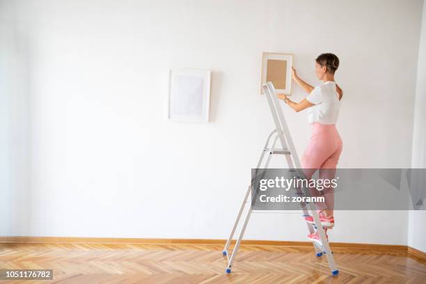 woman putting pictures on the wall - hanging artwork stock pictures, royalty-free photos & images