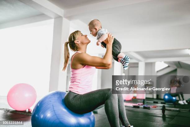 athlete mother playing with baby while resting from workout in gym - baby studio stock pictures, royalty-free photos & images