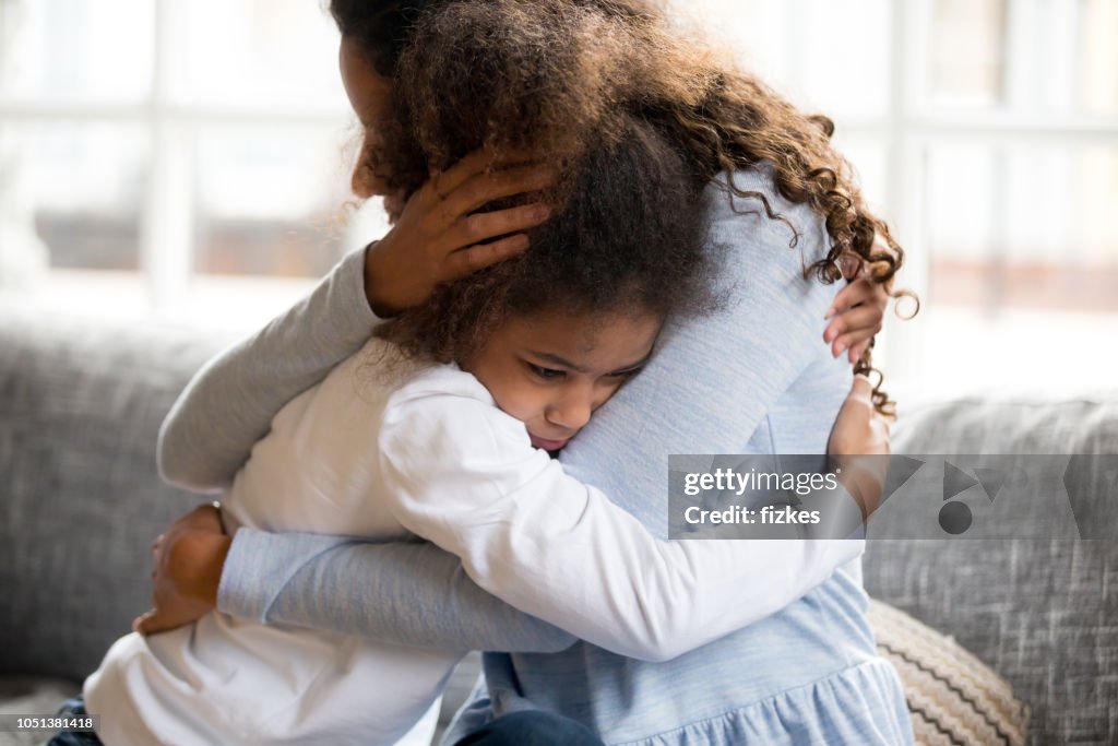 Negro madre e hija abrazando sentada en sofá