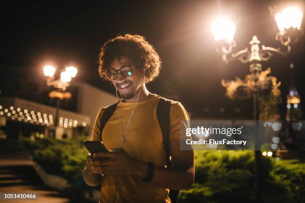 moderne zwarte student sms op zijn mobiele telefoon en glimlachen bij nacht - avondschool stockfoto's en -beelden
