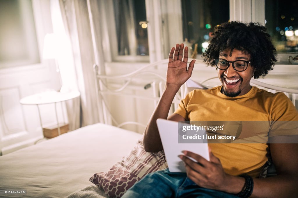 Smiling man lying in bed looking at a digital tablet
