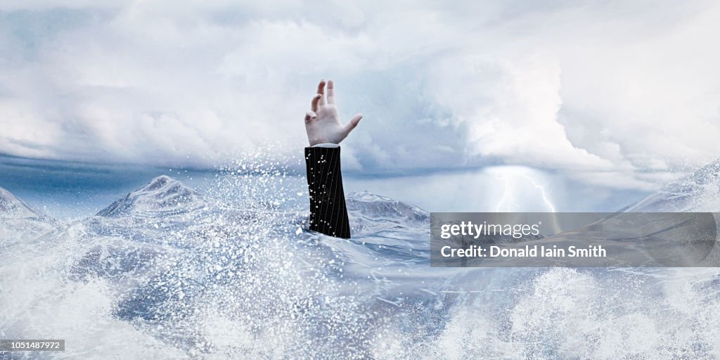 Hand of businessman raised in ocean with rough waves