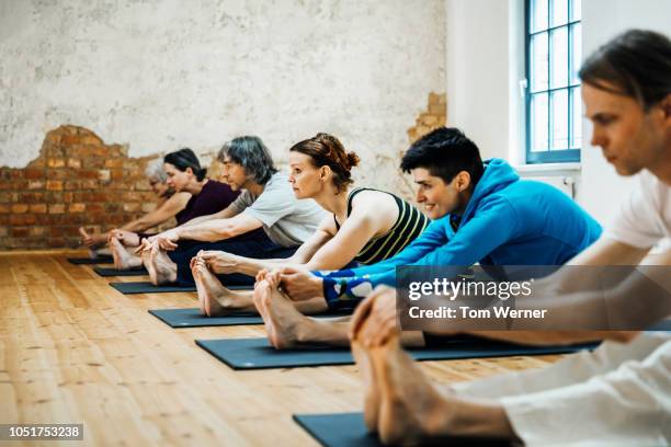 yoga class stretching on mats - touch toes stock-fotos und bilder