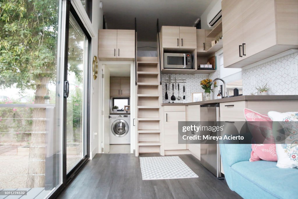 The interior of a tiny house with large glass windows, showcase the kitchen, living room and loft bedroom.